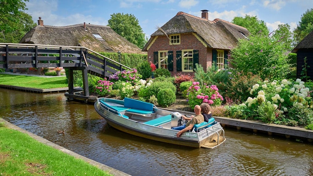 Boat ride on Giethoorn canal passing traditional Dutch house and garden, Netherlands.