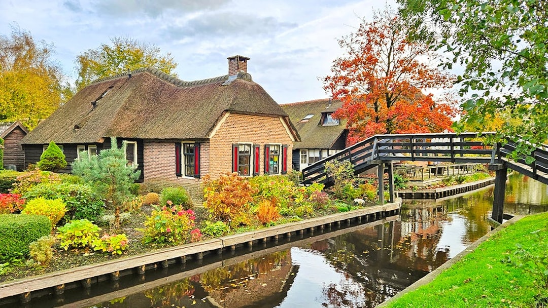Thatched-roof house and wooden bridge over canal in Giethoorn, Netherlands.