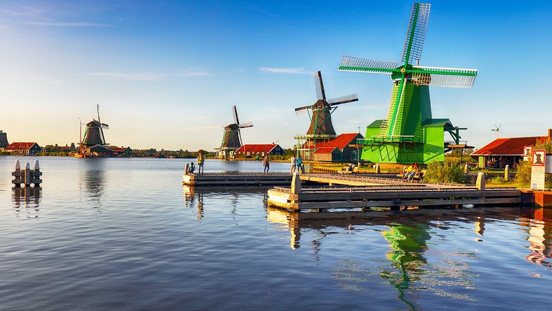 Windmills at Zaanse Schans near Amsterdam with people on a dock.