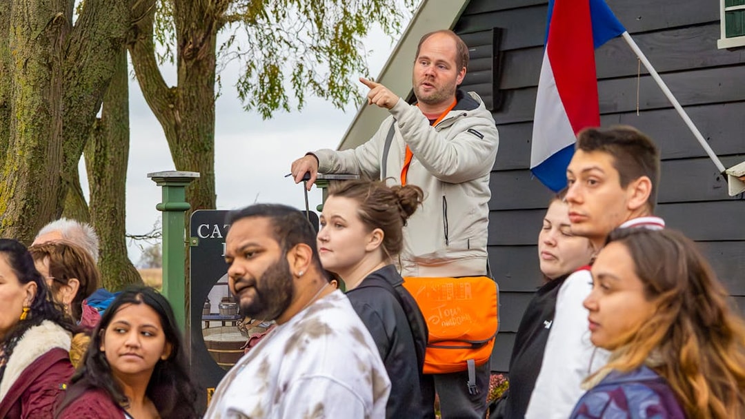 Tour guide leading visitors at Keukenhof with Dutch flag in background.