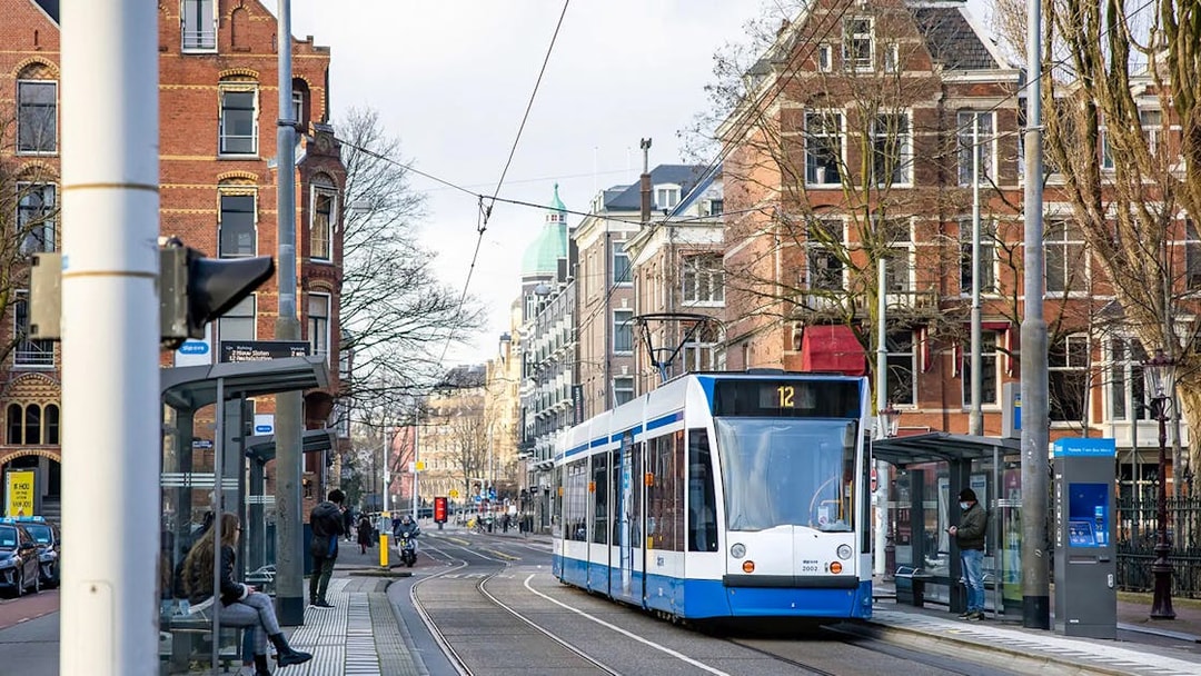 Tram in Amsterdam city center near historic buildings, showcasing public transport.