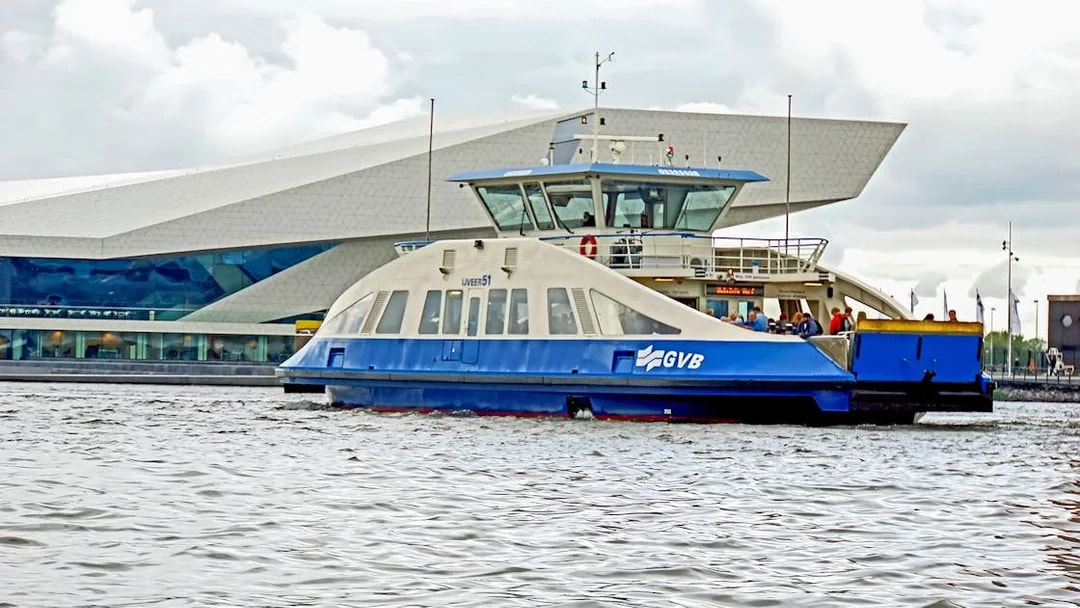 GVB ferry on Amsterdam canal near modern building.
