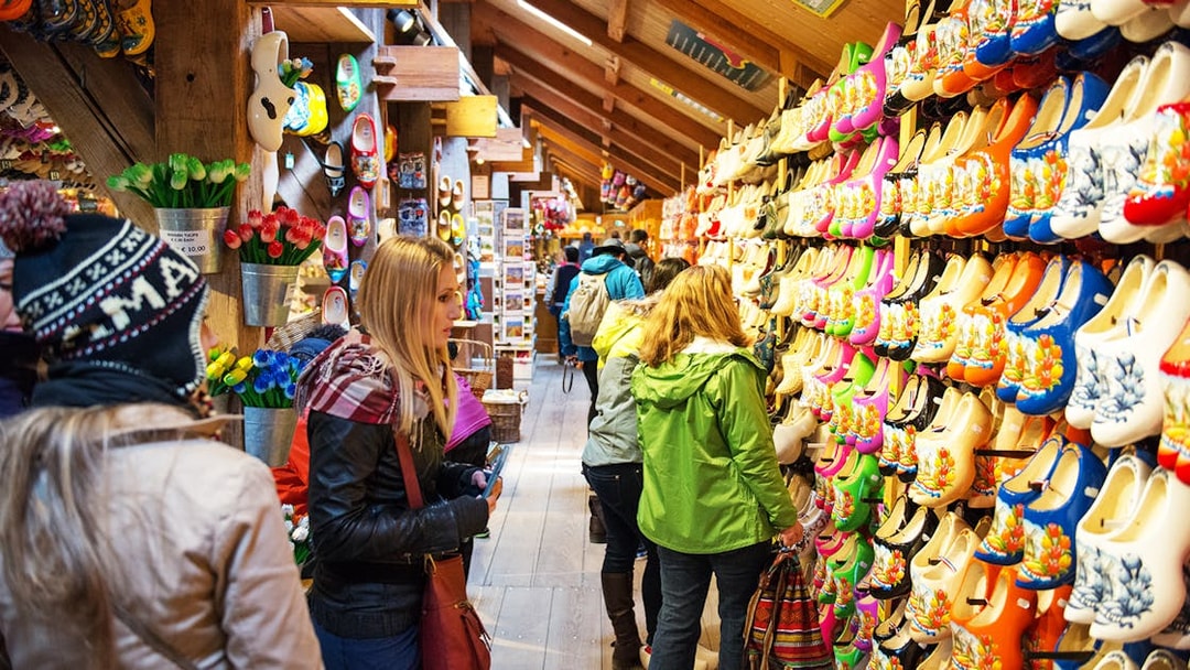 Visitors browsing colorful wooden clogs at a shop in Zaanse Schans, Netherlands.