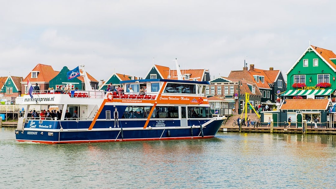 Tourists on a Marken Express boat cruise past colorful Dutch houses in Volendam.