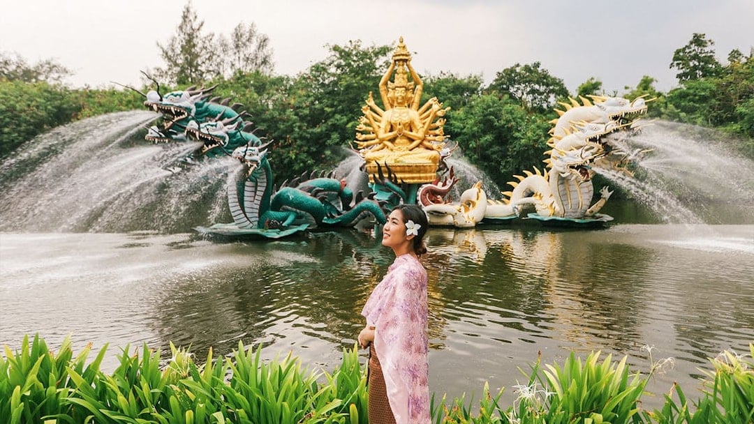 Woman in traditional attire at Erawan Museum with dragon sculptures and golden deity statue.