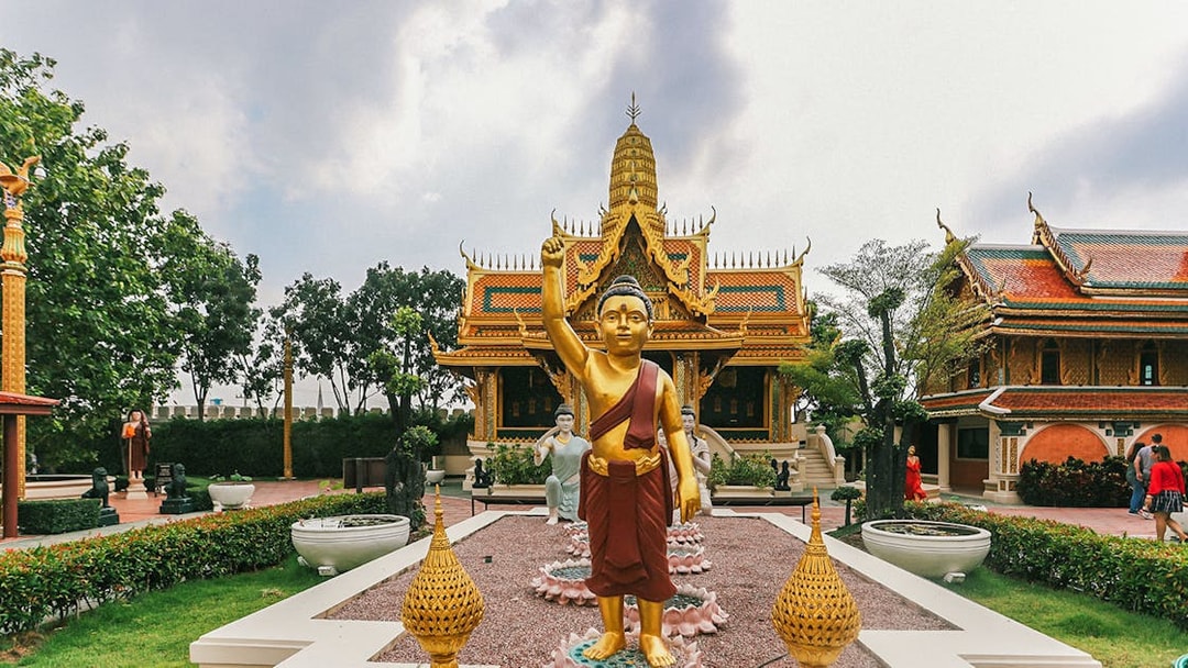 Golden Buddha statue at Erawan Museum with ornate temple in background, Ancient City tour.