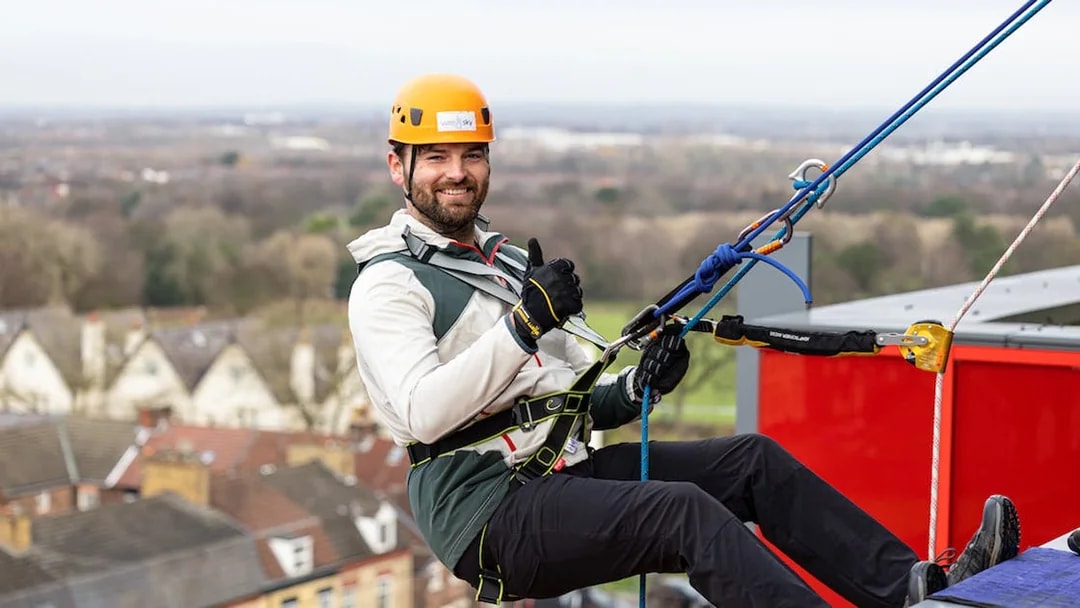Man abseiling at Anfield Stadium, Liverpool, with city view in background.