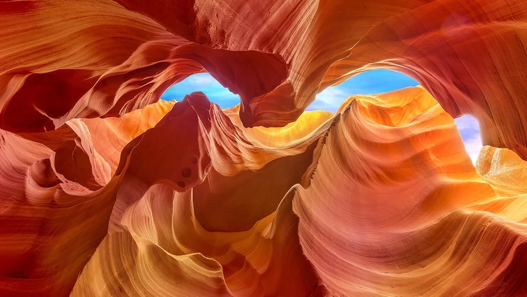 Lower Antelope Canyon's swirling sandstone formations under a blue sky.
