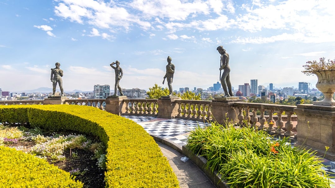 Chapultepec Castle terrace with historic statues overlooking Mexico City skyline.