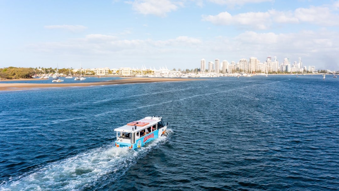 Aquaduck vehicle cruising on a river with city skyline in the background.