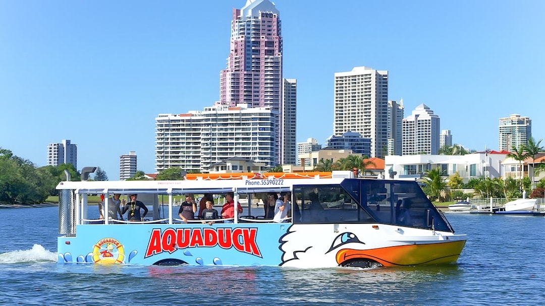 Aquaduck amphibious vehicle cruising on a river with city skyline in the background.