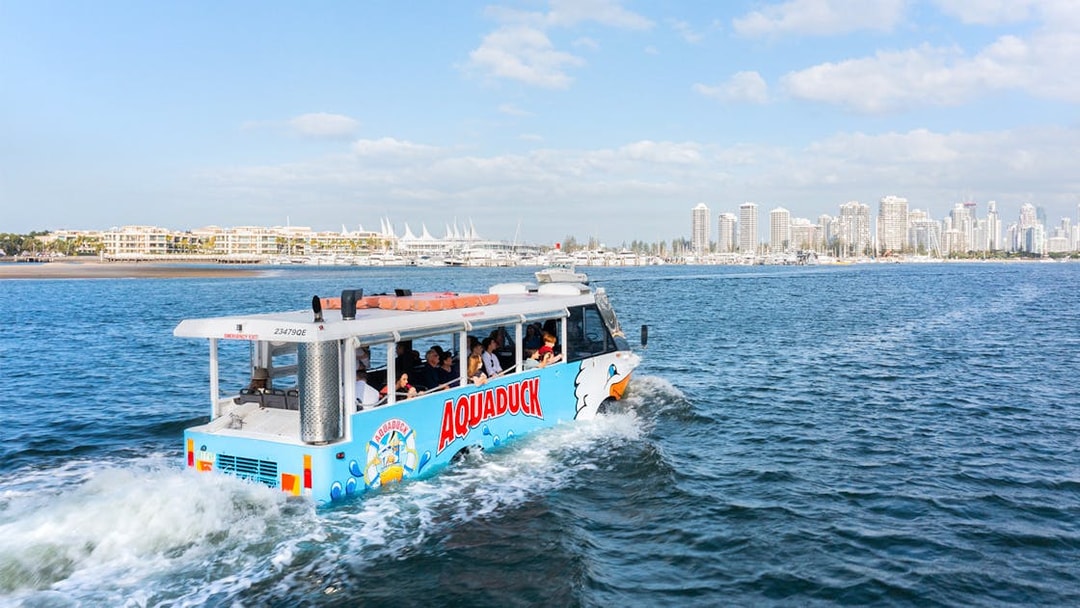 Aquaduck tour vehicle cruising on a river with city skyline in the background.