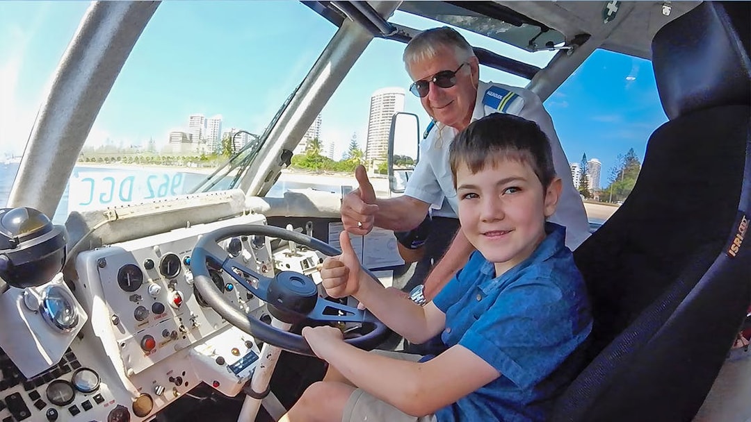 Child and guide giving thumbs up inside Aquaduck vehicle, Sunshine Coast skyline visible.