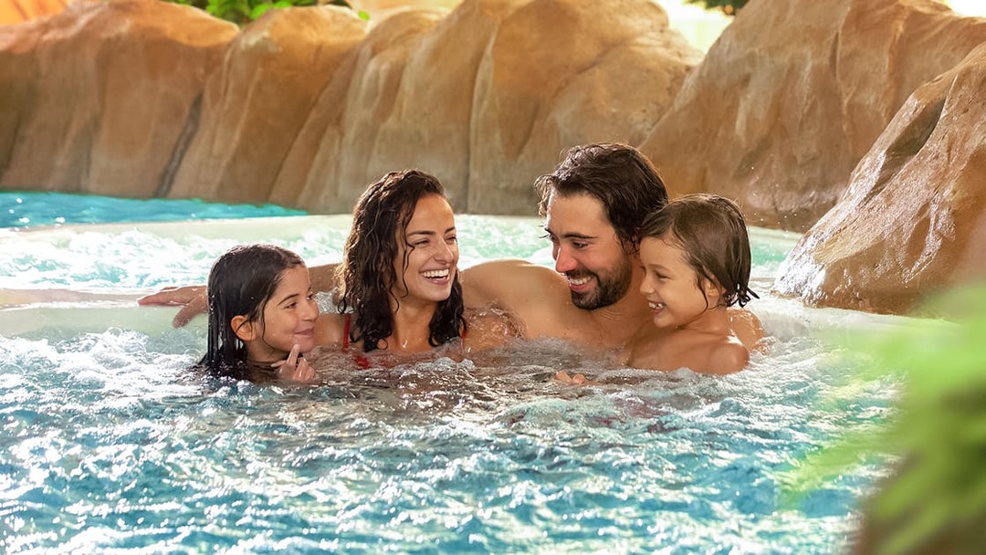 Family relaxing in a pool at Aqualibi, surrounded by rocks and greenery.