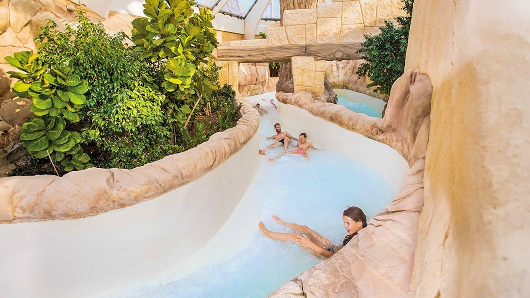 Tourists sliding down the Rapido slide at Aqualibi, surrounded by lush greenery.