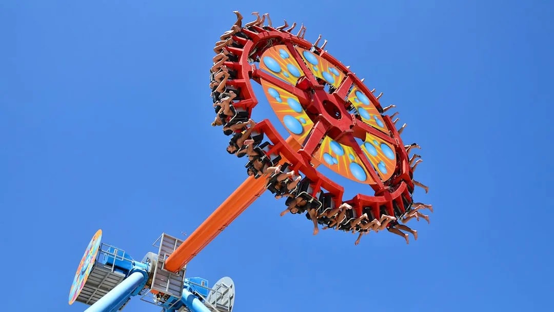 Visitors on a spinning ride at Aquashow Park against a clear blue sky.