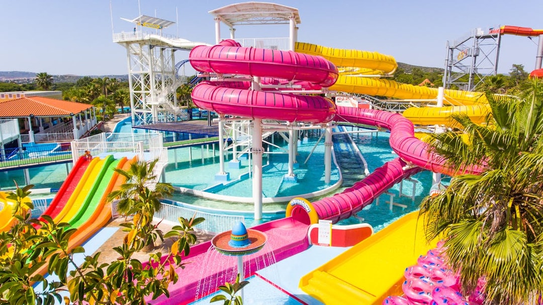 Colorful water slides at Aquashow Water Park, Portugal, with palm trees and clear blue pools.