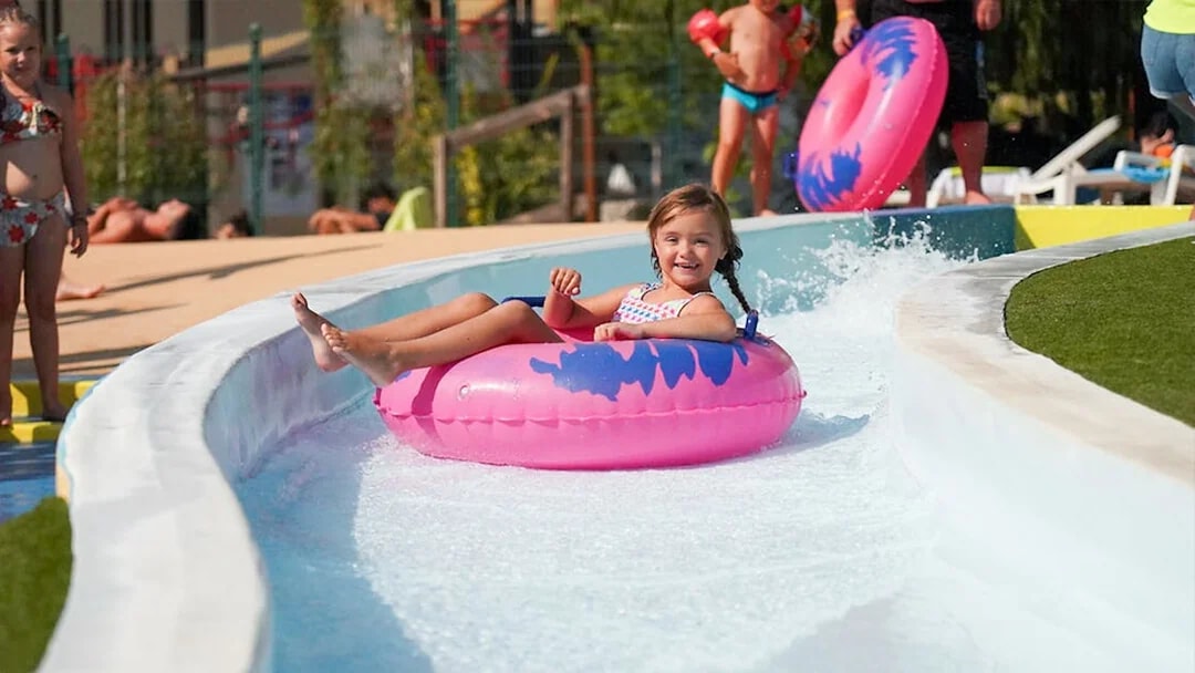 Child enjoying a water slide on a pink tube at Aquasplash Antibes.