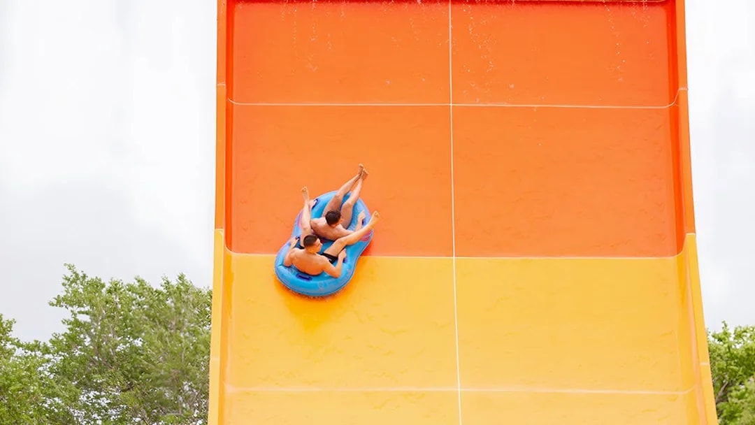 Two people on a blue raft sliding down a large orange water slide at Aquasplash Antibes.