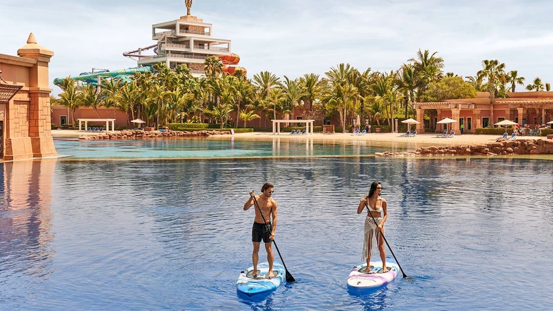 Tourists paddleboarding at Atlantis, The Palm, Dubai with water slides in the background.
