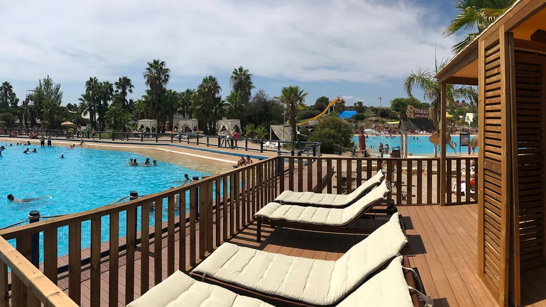 Sun loungers by the pool at Aquopolis Costa Daurada with water slides and palm trees in the background.