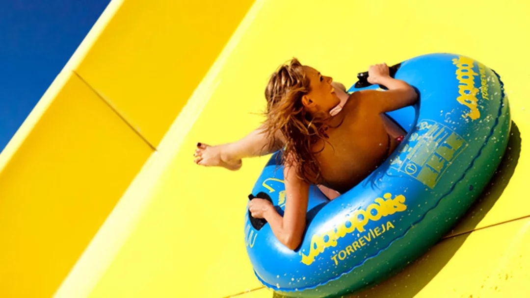 Person sliding on a yellow water slide at Aquopolis Torrevieja in a blue inflatable tube.