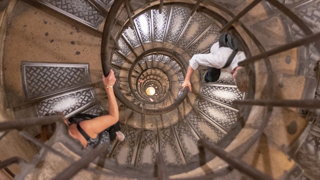 Visitors ascending spiral staircase to Arc de Triomphe rooftop, Paris.