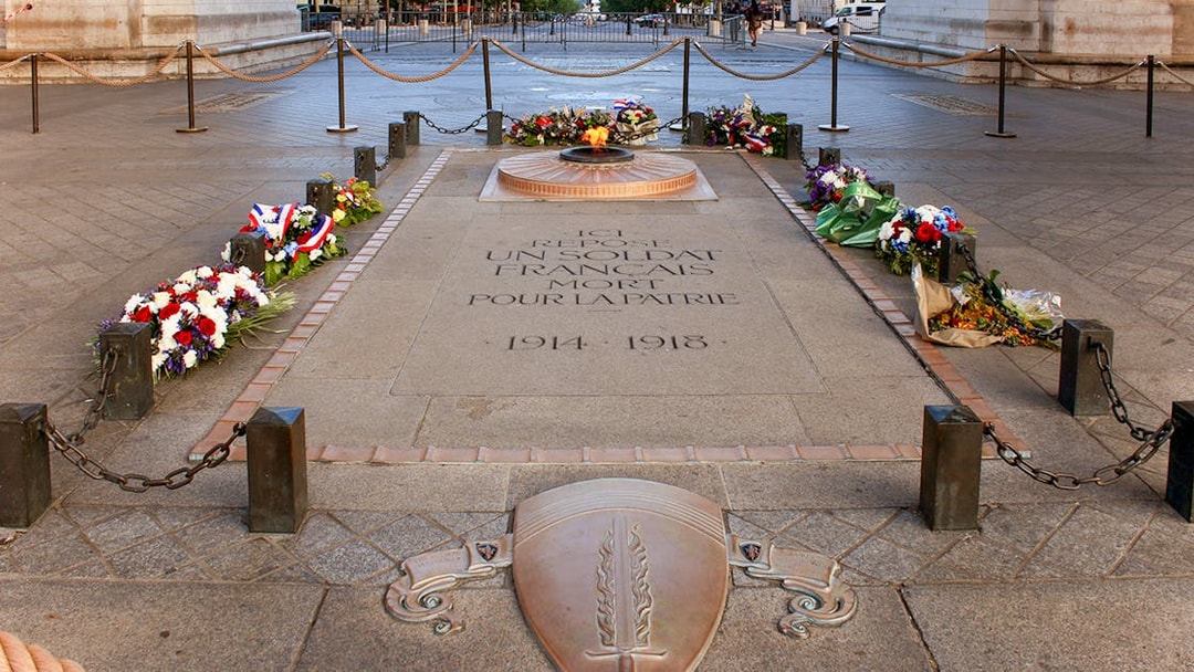 Unknown soldier's grave with eternal flame at Arc de Triomphe, Paris, surrounded by flowers.