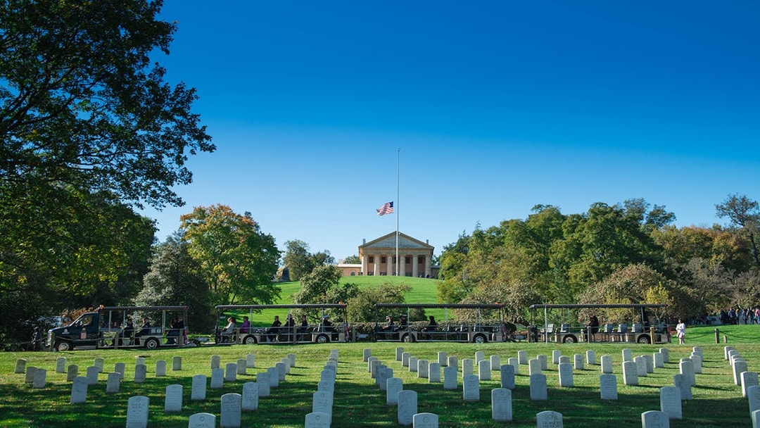 Tour tram passing Arlington National Cemetery graves with Arlington House in the background.