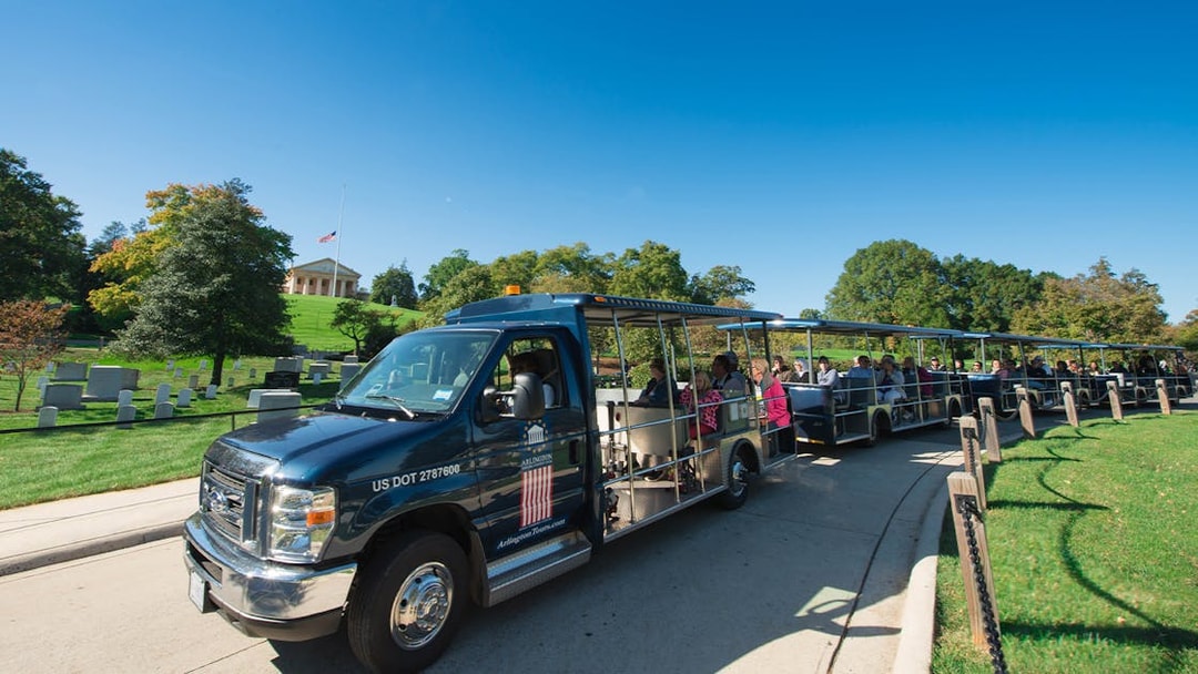 Tour tram at Arlington National Cemetery with visitors and headstones in view.