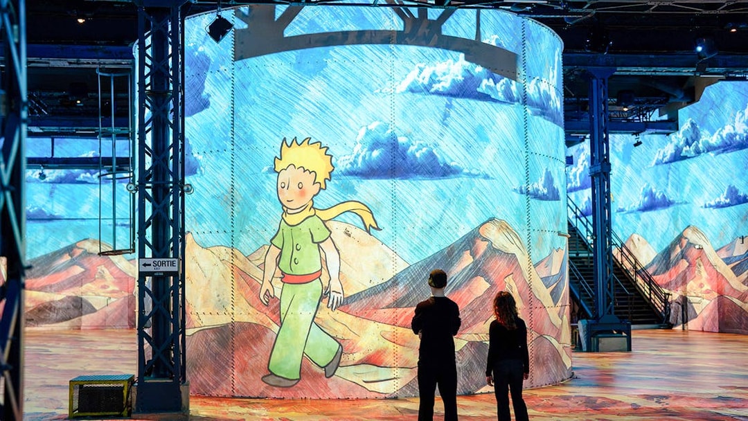 Visitors viewing Little Prince artwork at Atelier Des Lumières, Paris exhibition.