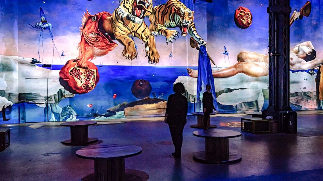 People viewing digital art projection at Atelier des Lumières, Paris, featuring surreal imagery.