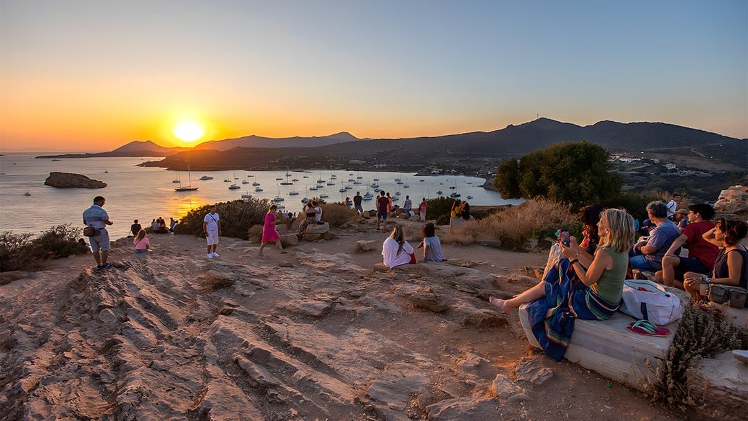 Tourists watching sunset at Archaeological Site of Sounion with sea and boats in view.
