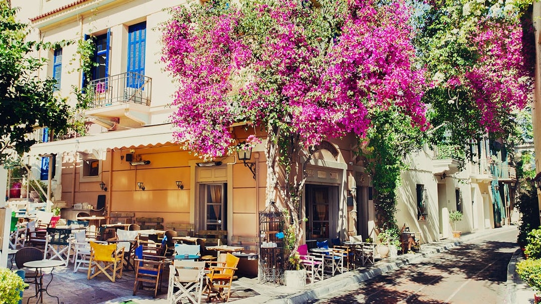 Outdoor cafe with colorful chairs and bougainvillea in Athens, Greece, on a street food tour route.