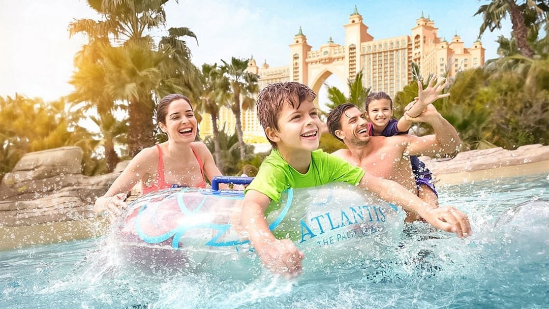 Family enjoying water ride at Atlantis The Palm with iconic hotel in background.