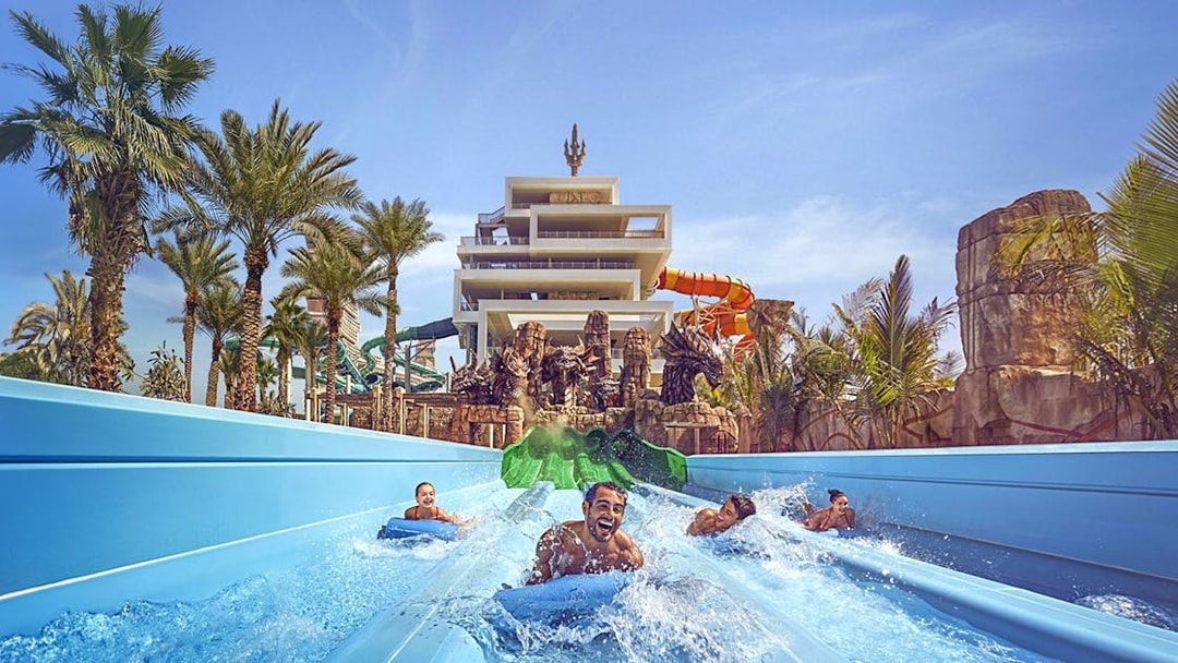 Visitors enjoying waterslides at Aquaventure Waterpark, Dubai, with palm trees and a tower in the background.