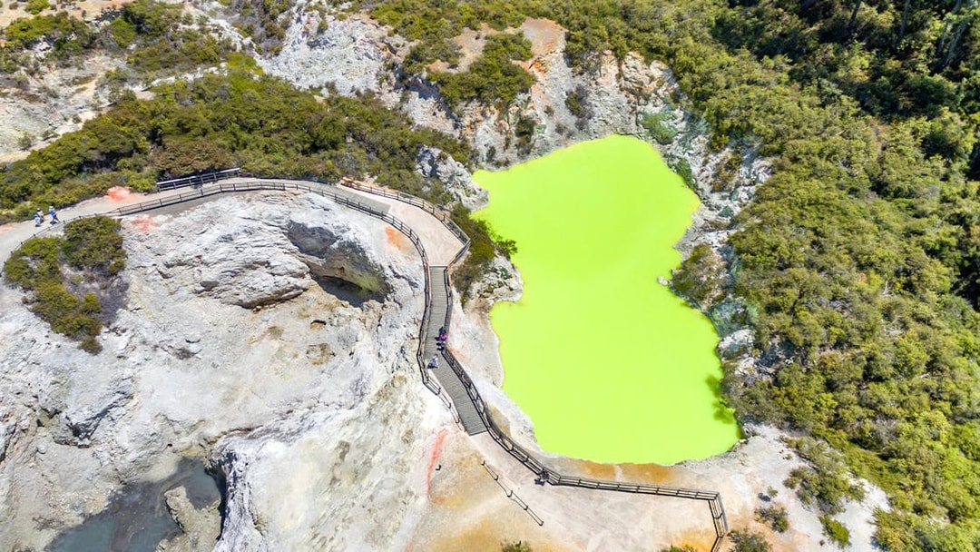 Aerial view of a vibrant green geothermal pool with a boardwalk in Rotorua, Auckland.