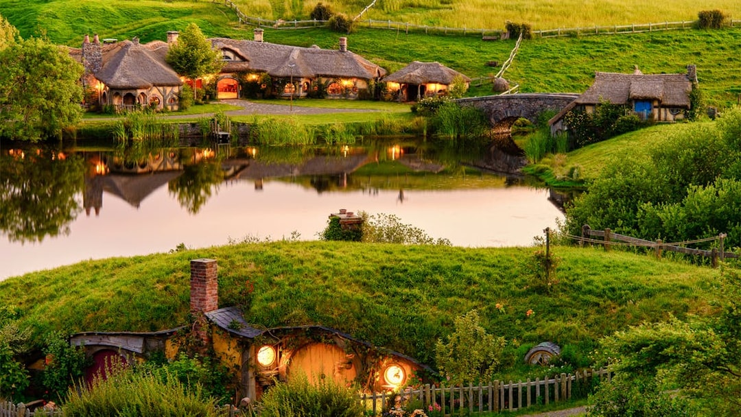 Hobbiton movie set with thatched cottages and lush green hills, part of Rotorua & Wai-O-Tapu tour from Auckland.