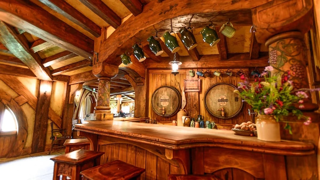Green Dragon Inn interior with wooden bar and hanging mugs at Hobbiton movie set.