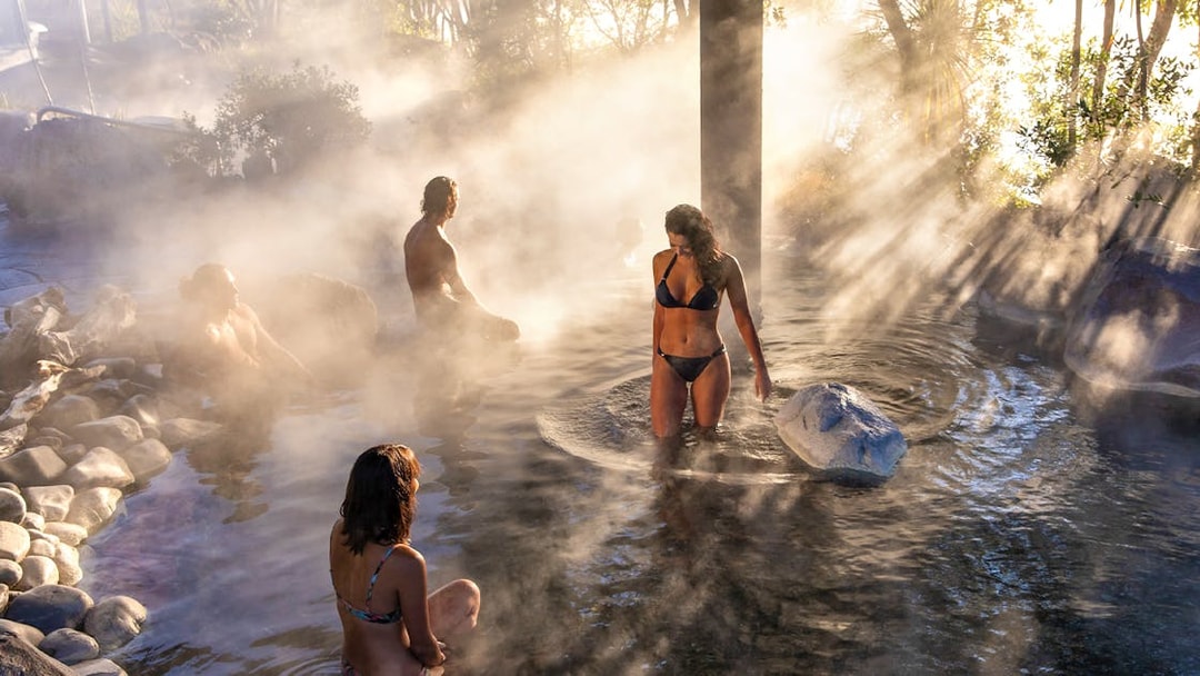 People enjoying geothermal hot springs at Te Puia, Rotorua, surrounded by steam and natural rock formations.