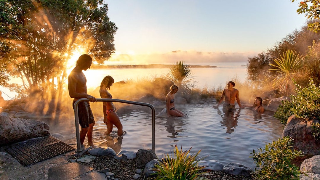 People enjoying a geothermal hot pool at sunrise in Rotorua, New Zealand.