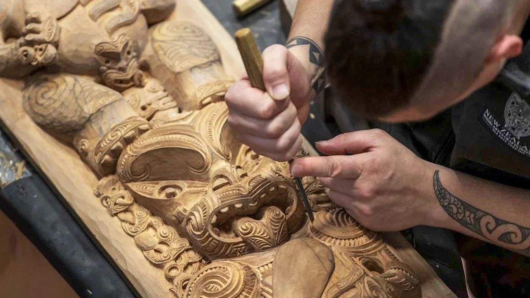 Carver working on intricate Māori wood carving at Te Puia, Rotorua.