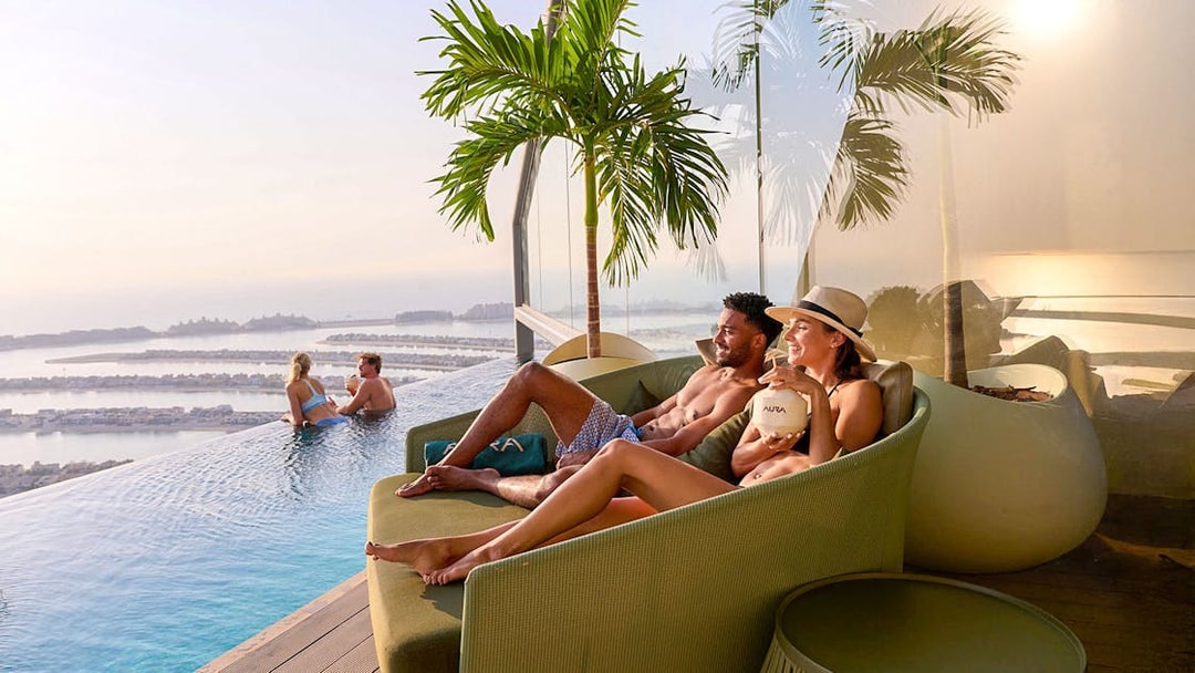 Couples relaxing by the pool at AURA Sky Pool with a view of Palm Jumeirah.