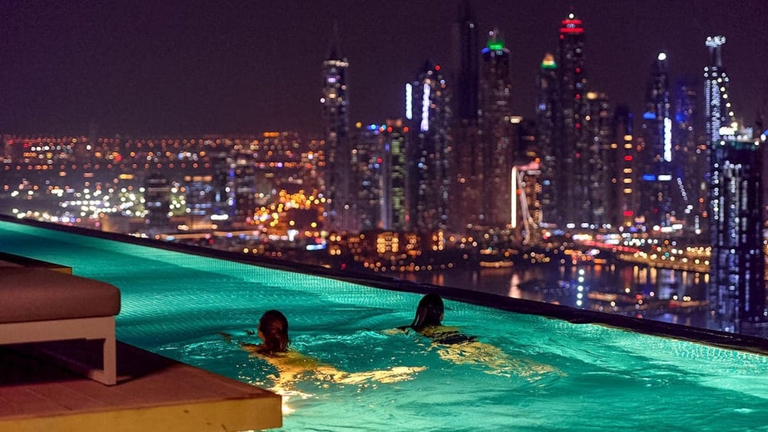 Tourists swimming at Aura Sky Pool with Dubai skyline at night.