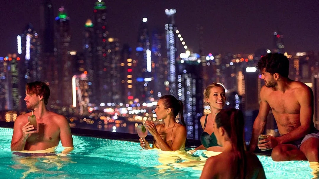 Tourists enjoying Aura Sky Pool with Dubai skyline at night.
