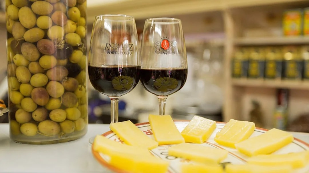 Red wine glasses, cheese slices, and olives on a Lisbon food tour.