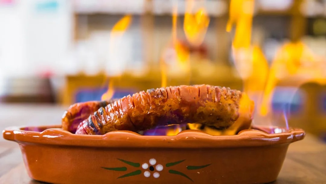 Grilled chorizo sausage on fire in a traditional clay dish, Lisbon food tour.