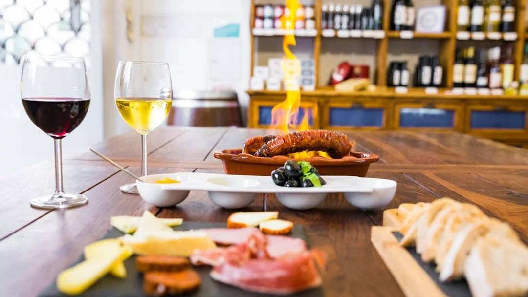 Lisbon food and wine tour with flaming chorizo, cheese, olives, and wine glasses on a wooden table.