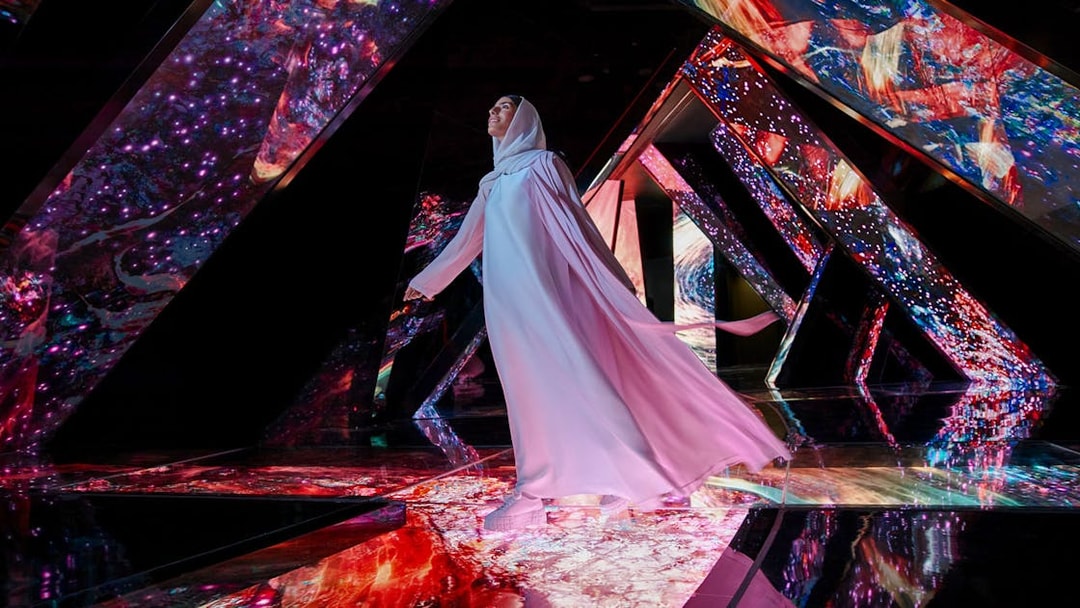 Person walking through a vibrant, mirrored installation at AYA Universe.