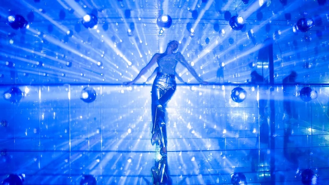 Person in reflective outfit at Harmonia zone, AYA Universe, Dubai with blue light beams.